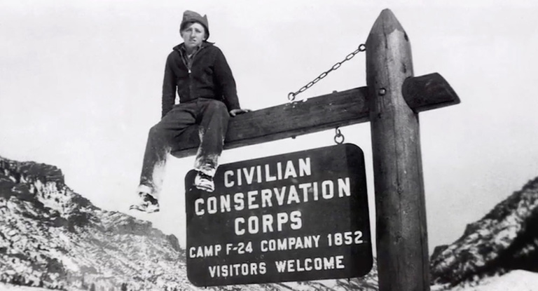 A boy sits on a Civilian Conservation Corps sign