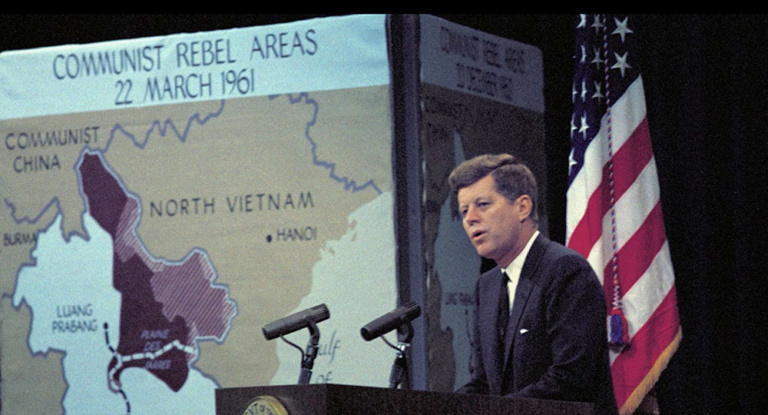 President John F. Kennedy stands at a podium in front of a map of Vietnam