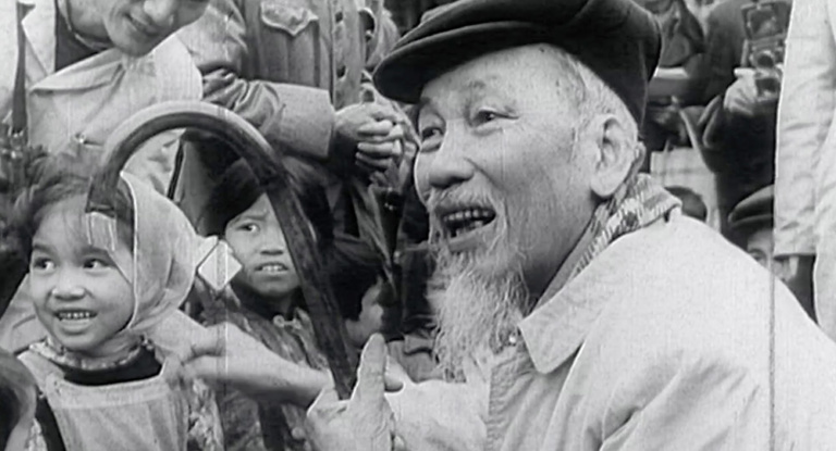 An older Ho Chi Minh crouches to greet children.