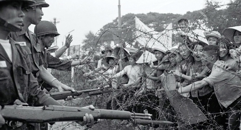 South Vietnamese soldiers point guns at a crowd, separated by barbed wire.